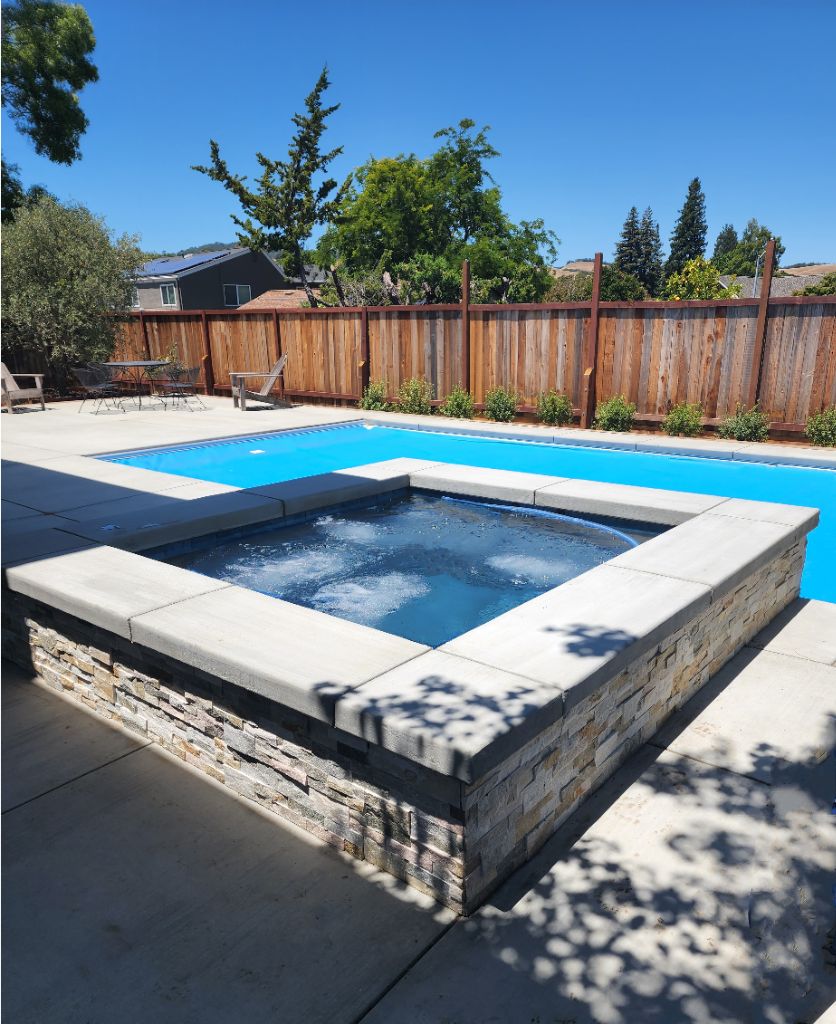 Rectangular shaped pool with a blue automatic pool cover and raised spa with ledgerstone and concrete cap.