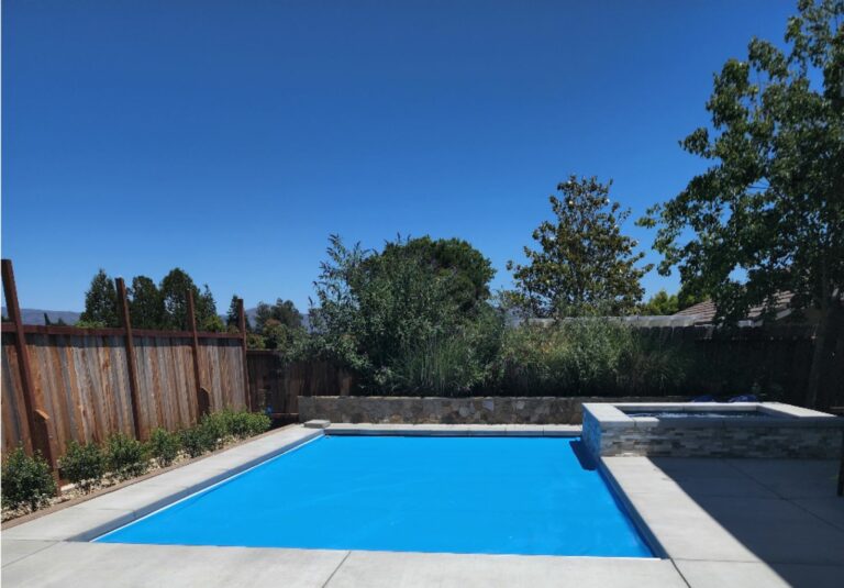 Rectangular shaped pool with a blue automatic pool cover and raised spa with ledgerstone and a stone faced retaining wall planter.