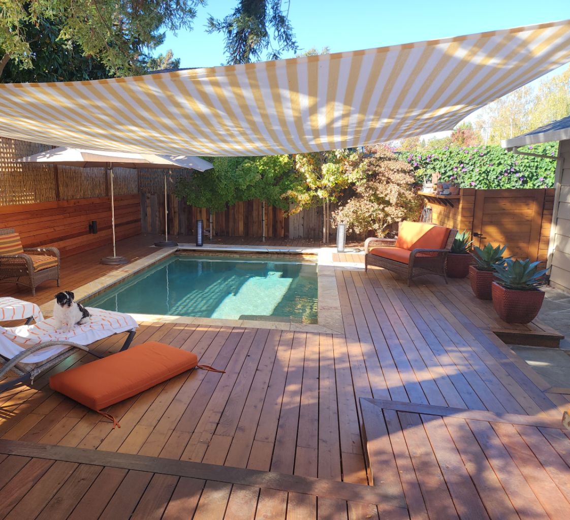 Small rectangular pool with an automatic pool cover and wood decking and a stiped awning.