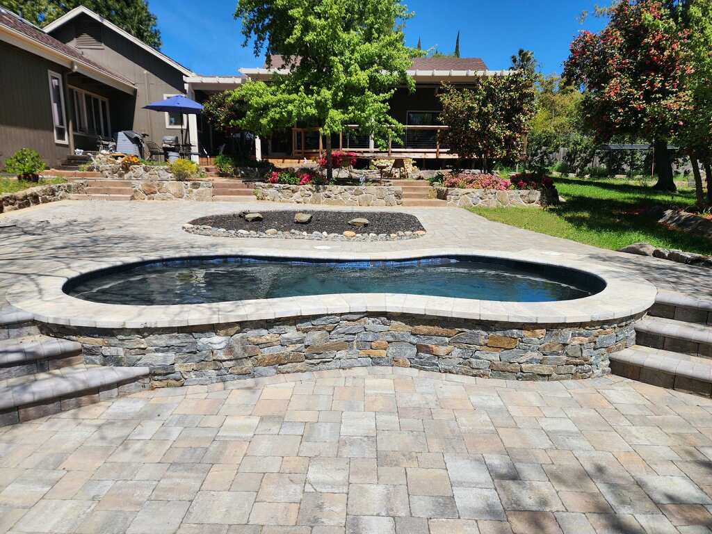 Partially raised small freeform shaped pool iwth stone and paver decking