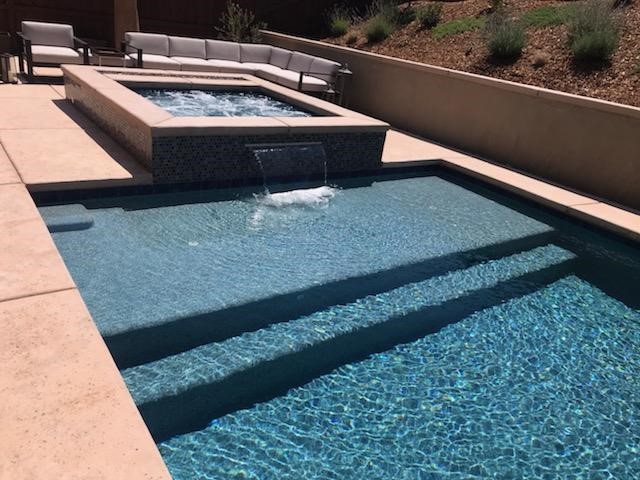 Raised spa with a sheer descent water feature into rectangular shaped pool with large Cabo shelf.