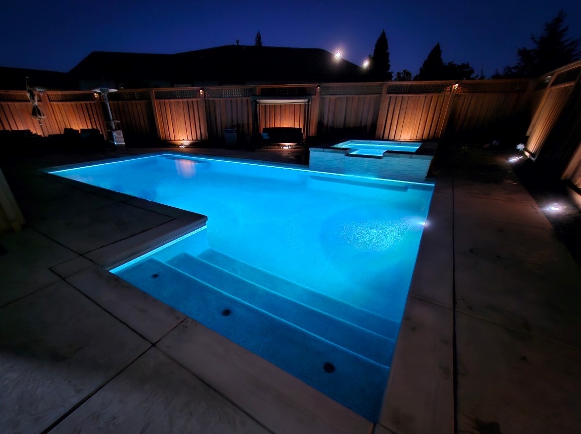 Rectangular pool with raised spa and bumped out Cabo shelf and entry steps at night with lights