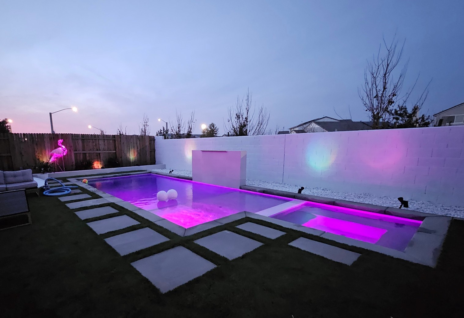 Rectangular pool with spa and raised wall with sheer descent and colored LED lighting at night