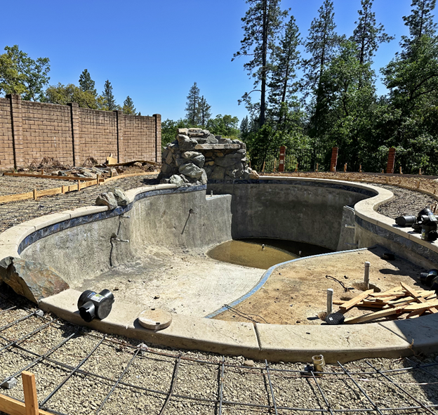 A freeform pool under construction with a large rock waterfall in Auburn