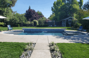 Concrete walkway leading to custom backyard pool installation.